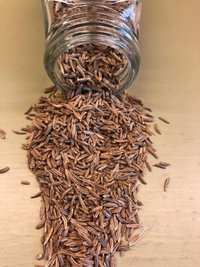 Overturned glass jar with caraway seeds spilling out