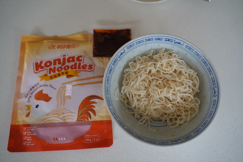 A bowl of konjac noodles in a white bowl with a blue rim, next to a package of noodles with a rooster on the cover